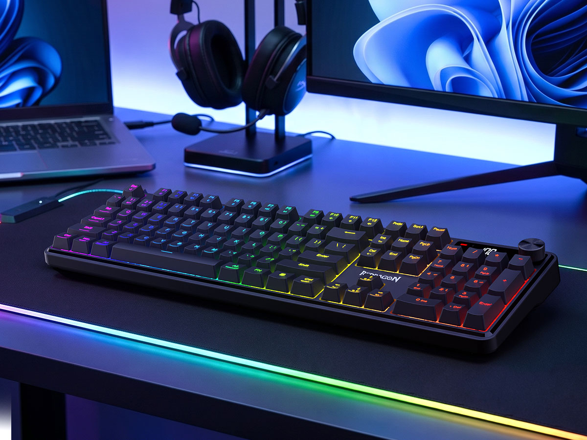A black mechanical gaming keyboard with RGB backlighting sits on a desk in a styled setup, with a...